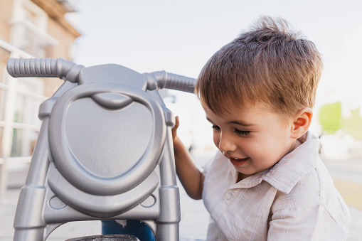 Boy smiles as he crouches next to his toy motorcycle pretending to be repairing it. He looks away