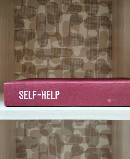 Photo of Book on book shelf with text SELF-HELP, concep of self-help book that is written to instruct its readers on solving personal problems - classified as Self-improvement books