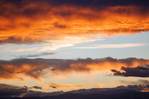 An airplane disappears into the distance as the golden light of the setting sun casts an orange glow on the dark clouds.