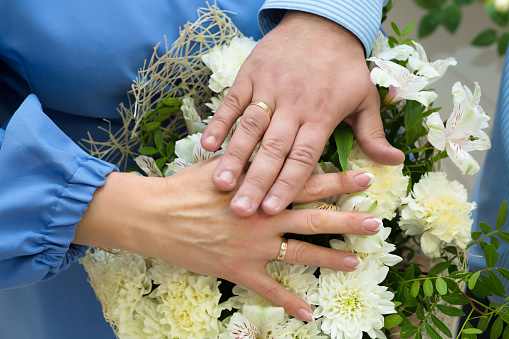 Hands of  bride and groom with wedding rings on background of a bouquet chrysanthemums and white lilies.