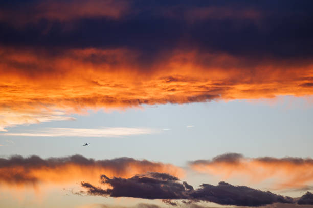 An airplane disappears into the distance as the golden light of the setting sun casts an orange glow on the dark clouds.