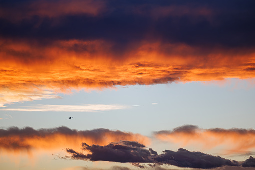 An airplane disappears into the distance as the golden light of the setting sun casts an orange glow on the dark clouds.