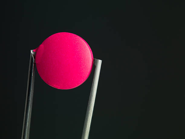 istock pink pill in tweezers 184229400