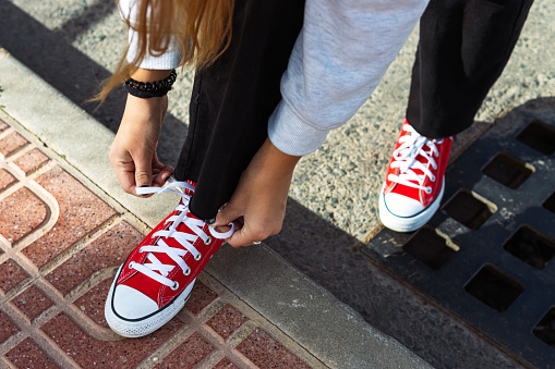 the legs of a beautiful teenage girl. Young hipster woman tying laces in red sneakers. Sunny hot summer day