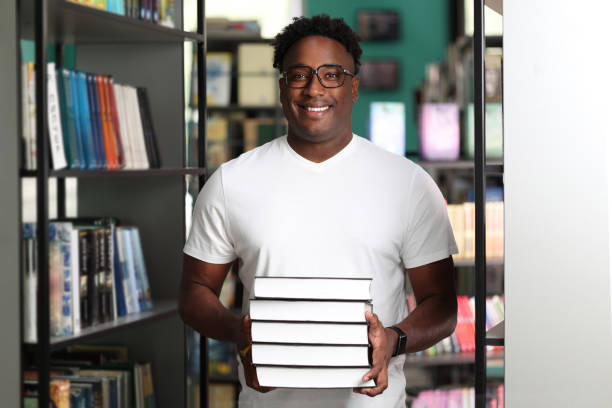 istock Positive student preparing for exams in library, collected heavy stack of books 1842353464