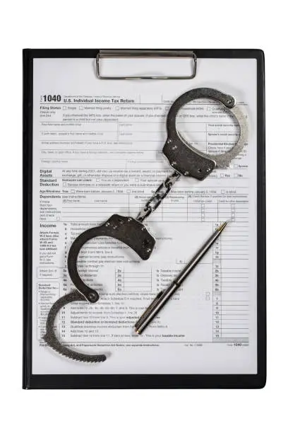 Photo of Handcuffs over Tax forms, concepts: Tax fraud or Slave to the Taxes