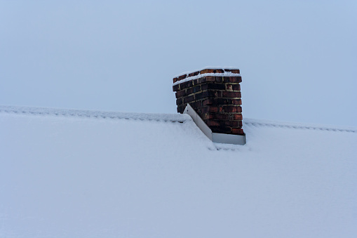 A snow-capped chimney made of red bricks in winter.