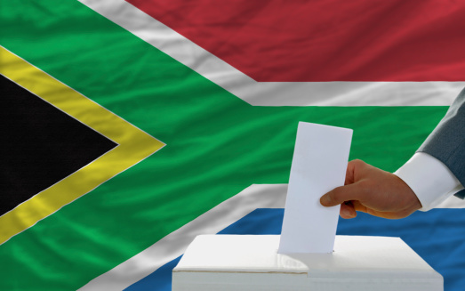 man putting ballot in a box during elections in south africa in front of flag