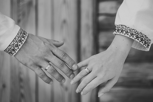 Hands are newlyweds with wedding rings. Rings and engagement. Bride and groom wearing embroidered dress and shirts hold hands together closeup. The Bride and groom holding hands. Black and white photo