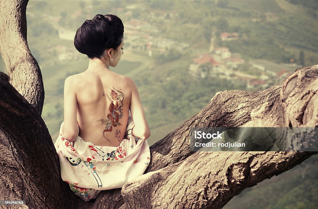 Woman with snake tattoo on the tree branch Asian style portrait of young woman with snake tattoo on her back sitting on the tree branch Tattoo Stock Photo