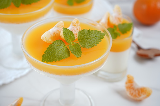 Vanilla panna cotta with tangerine layer in a small portioned vase and fruit pieces in wineglasses. Delicious Italian dessert.