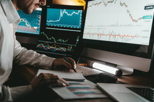 istock Close-up of male trader making notes and using computers while analyzing stock market data in night office 1842519390