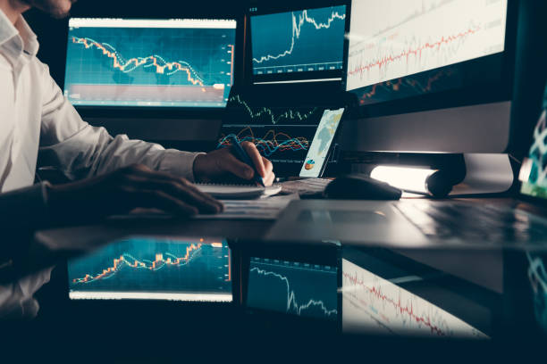 istock Close-up male trader analyzing stock market data while sitting at the office workstation with multiple computers 1842519491