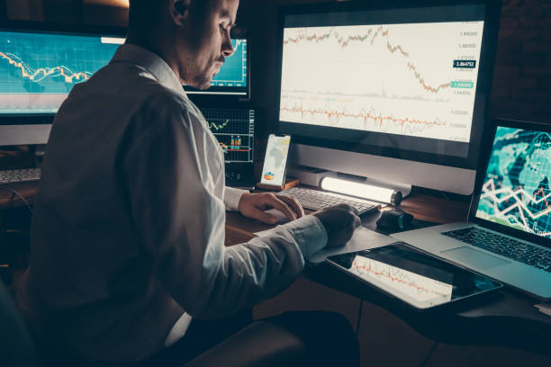 istock Close-up male trader analyzing stock market data while sitting at the office workstation with multiple computers 1842519558