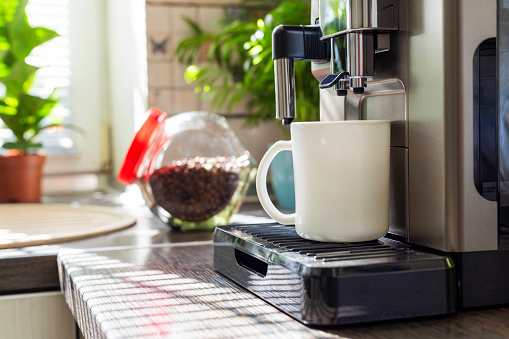 Modern electric coffee machine with cup on countertop in kitchen.