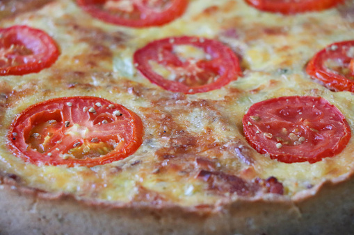Stock photo showing close-up, elevated view of a fluted pastry crust, homemade, Quiche Lorraine topped with tomato slices.