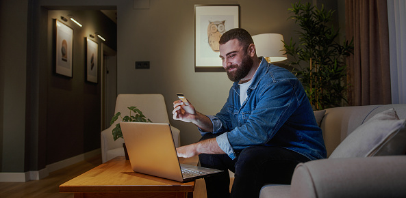 Man working on laptop at home during evening, comfortable and focused in a cozy living room setting.
