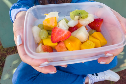 Photo of a woman holding a transparent plastic container with fruits.