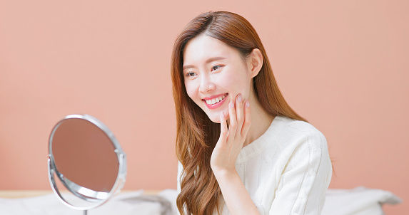Closeup view asian beautiful woman looks in the mirror feels happy that her facial skin is in good condition - autumn and winter care