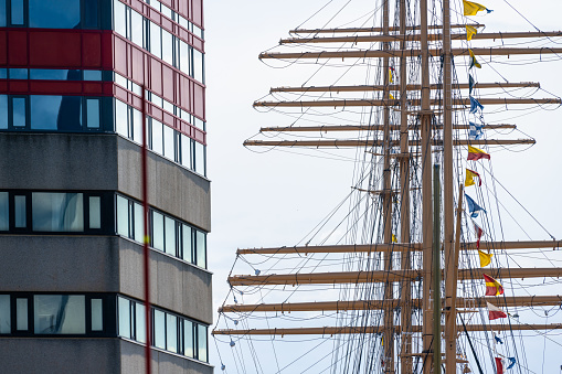 Gothenburg, Sweden - July 30 2023: Masts of a sailing ship in front of modern office building.
