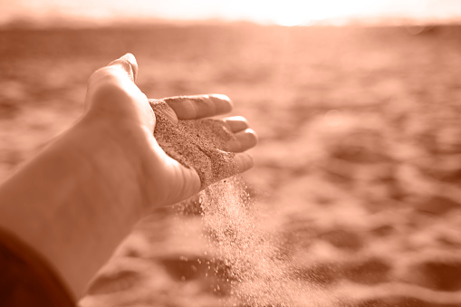 Close-up hand releasing dropping sand. Sand flowing through the hands. Trendy color of year 2024 - Peach Fuzz.