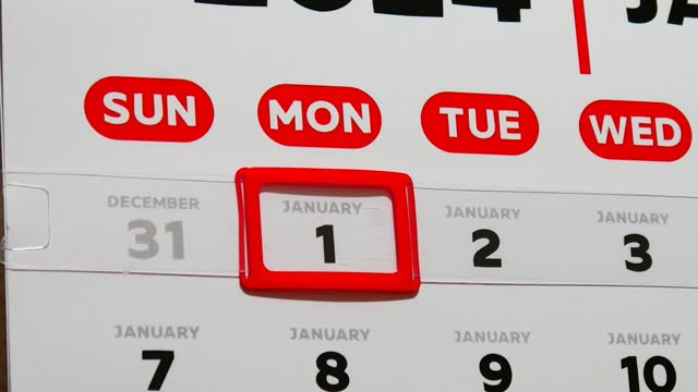 Close-up of a male finger moving a red cursor to the 1st January of the wall calendar 2024