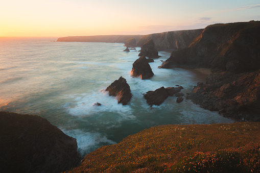 Dramatic seascape Atlantic coast landscape with sunset or sunrise golden hour light at Carnewas and Bedruthan Steps rock formations in North Cornwall, England, UK.
