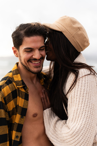 Vertical close-up portrait of a multi-ethnic couple embracing during a honeymoon on the beach