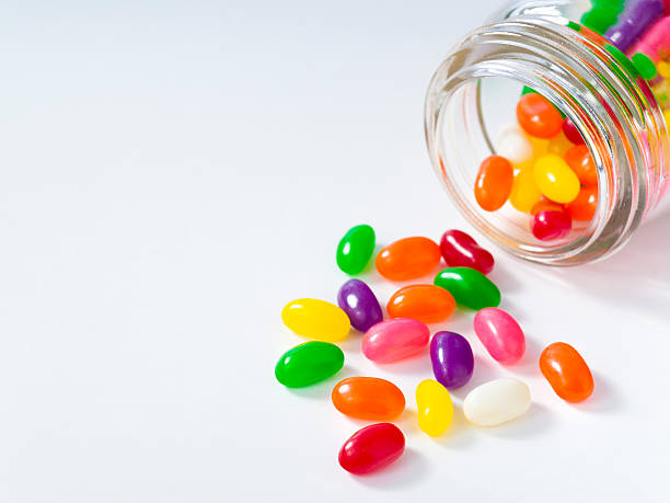 Jelly beans spill out of a jar Jellybean sugar candy snack fall from a glass container jellybean stock pictures, royalty-free photos & images