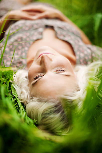 Young beautiful woman of 20s lying in the grass, looking at camera and smiling. Portrait only. 