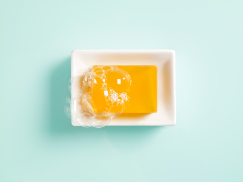 Orange bar of soap in a white ceramic dish on a light green background.