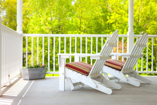 Two adirondack style chairs on a porch on a late Spring day