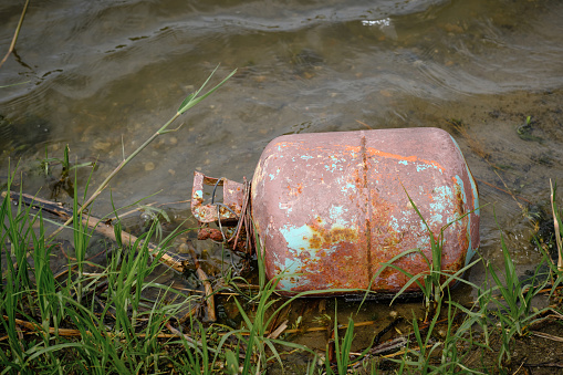 Old gas cylinder riverbank, pollution of ecology and nature