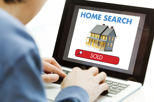 An unidentifiable man who is a real estate agent or consumer house hunter using a laptop computer for a home search online, seeing a sold property on the screen. He is buying or selling a house online, typing on the keyboard and shopping to find internet web real estate listings.