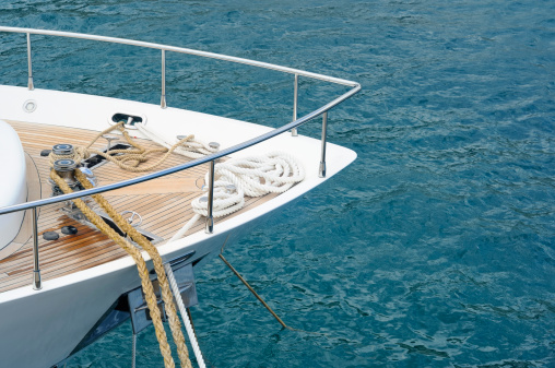 Bow of a motor yacht with teak deck moored in the harbor.