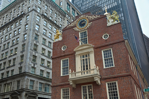 This is the east facade of Boston's red brick Old State House Museum with the balcony where Boston's first public reading of the Declaration of Independence took place. Golden lion and unicorn statues grace the roofline with a clock of elaborate ornamentation is mounted between them.