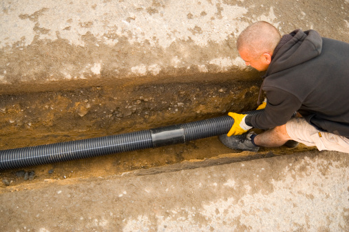 Shot of a road worker fitting drain pipes in a drainage ditch and connected the pipes to a sewer. Slight motion blur on the right end of the pipe