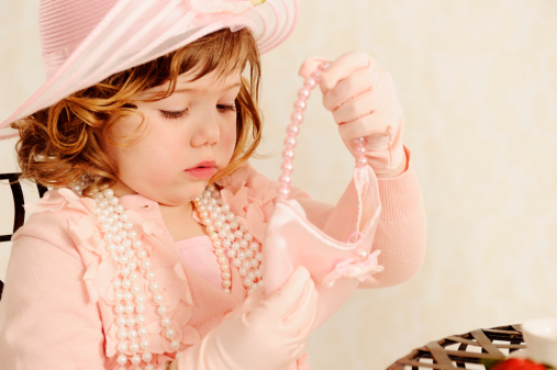 Delightful Little Girl Playing Dress ups and Tea Party.  Pretty pink hat with brim turned up and flower on it.  Lots of pearls and pink sweater and pink gloves.  Little girls lips in focus.  SDOF.  Antique looking. Copy space.