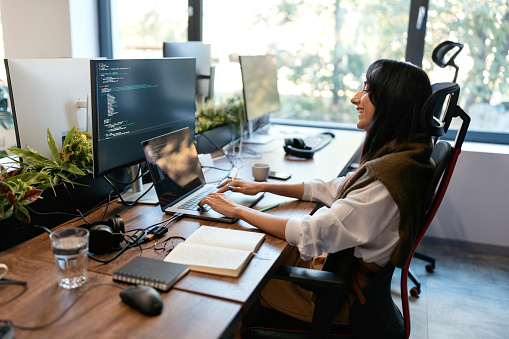 Beautiful, smiling woman coding on her computer in the modern company