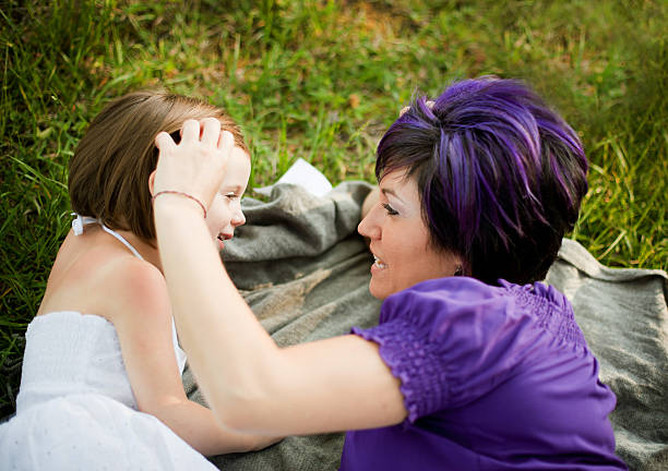 Mother and Young Daughter Talking While Outdoors Color image of a stylish mother laying in the grass on a blanket with her daughter laughing and bonding. purple hair stock pictures, royalty-free photos & images
