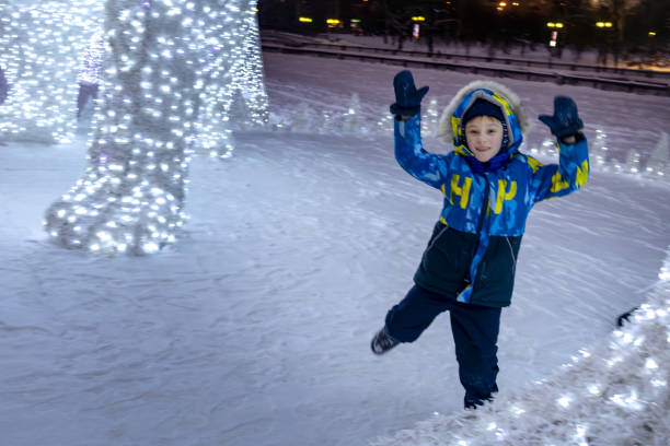 istock Boy in warm clothes plays next to Christmas installations, illuminated decorations in snow in evening. Skating. motion blur 1842703398