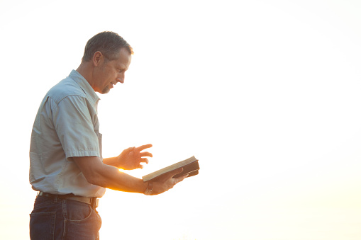 Pastor casually dressed walking in sunlight reading Bible
