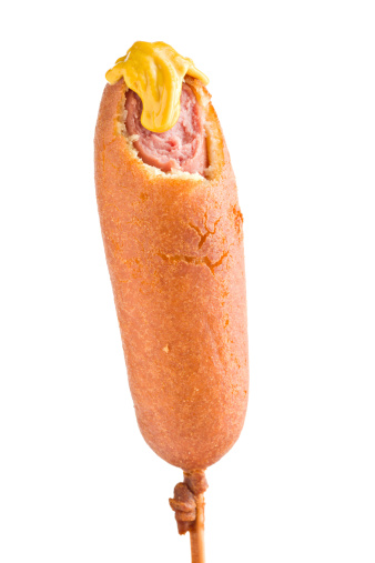 A close up of a golden brown corn dog on a stick with a bite missing and a dollop of yellow mustard. Isolated on white.