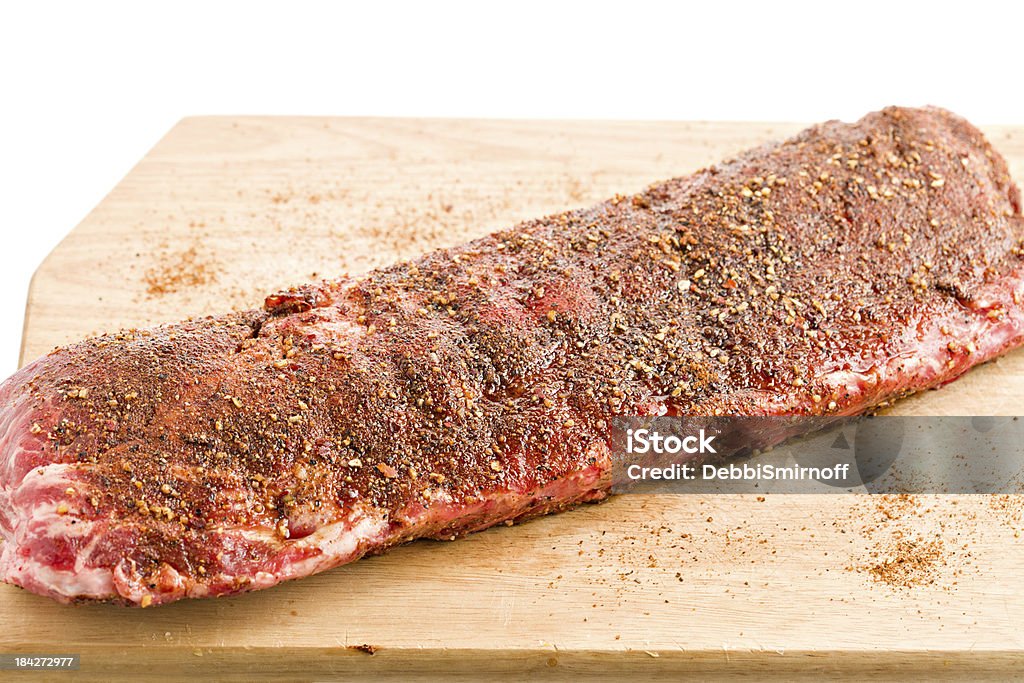 Cooking Pork Ribs "A high angle view of a slab of pork ribs on a wooden cutting board. The ribs have been dry rubbed with a Texas style rub consisting of brown sugar, cayenne pepper,chilli pepper, black pepper and cumin, it will be refrigerated overnight, into the oven at 300-350F for 2.5 Hrs and finished off in the smoker grill for another 1.5 Hrs. Isolated on white ." Rubbing Stock Photo