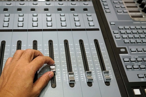 Sound engineer working on mixing console, closeup of hands doing adjust a fader.