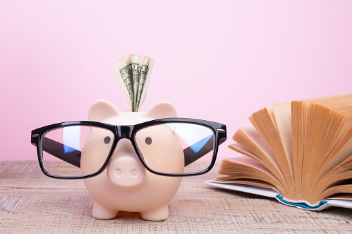 Piggy bank in glasses and books on pink background. open book. Tuition payment. Brainwork