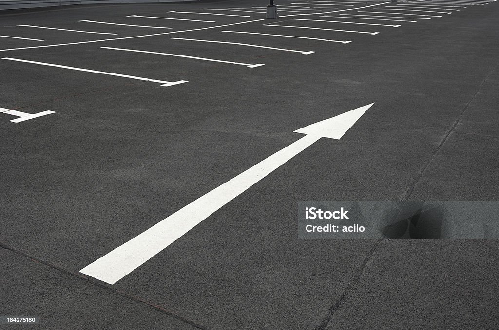 White arrow on an empty parking lot Arrow points the way on an empty parking lot. Parking Lot Stock Photo