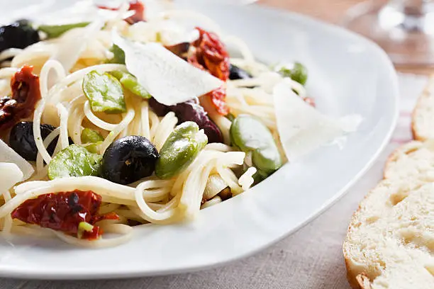 delicous pasta, plate with spagetthi, fresh green fava beans, dried tomatoes, olives and pecorino cheese