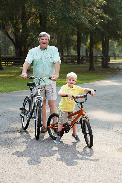 petit garçon d'équitation de vélo avec son grand-père - active seniors enjoyment driveway vitality photos et images de collection