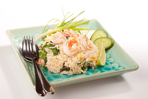 A plate of Thai prawn fried rice with traditional garnishing of spring onion, cucumber and lime.